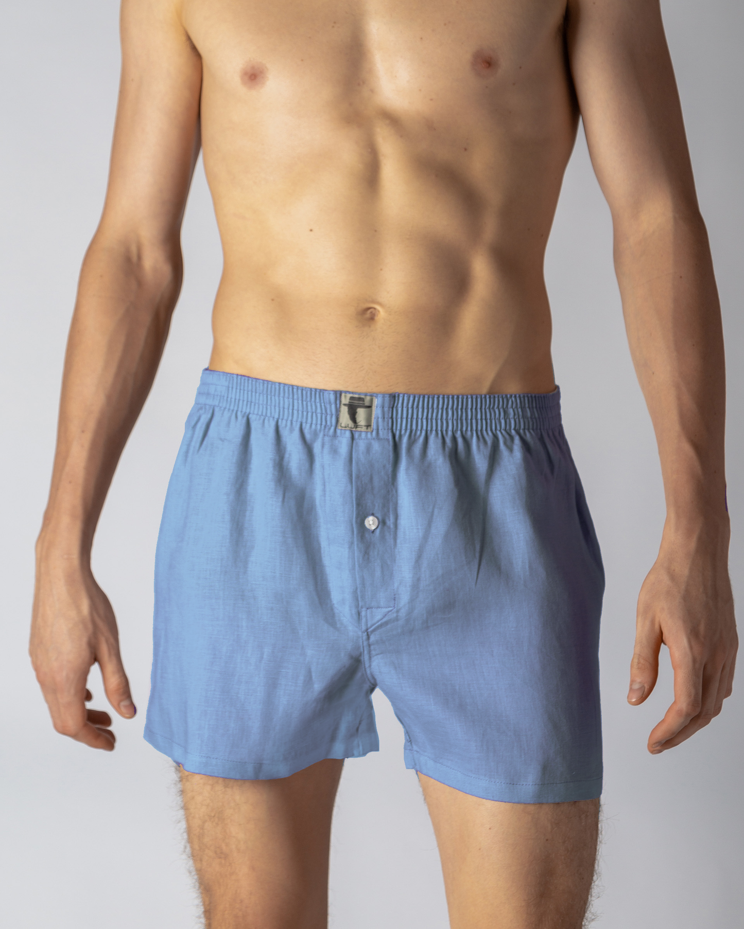 A model wearing blue 100% linen men's boxer shorts with a visible button fly front.